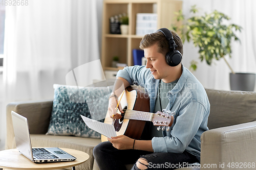 Image of man in headphones with guitar, notes and laptop
