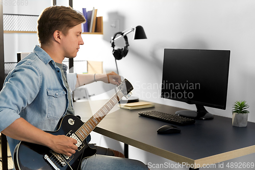 Image of young man with computer playing guitar at home