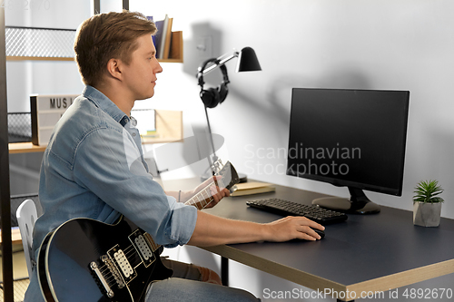 Image of young man with computer and bass guitar at home