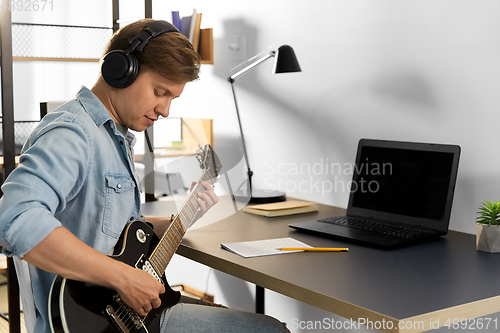 Image of man in headphones playing bass guitar at home