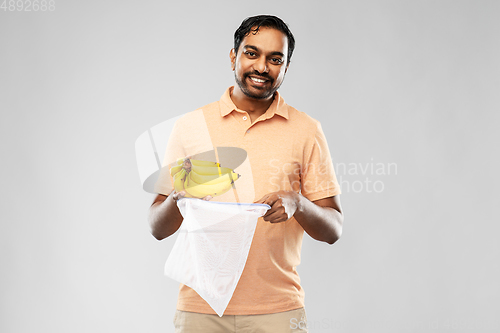 Image of happy man putting bananas into reusable string bag