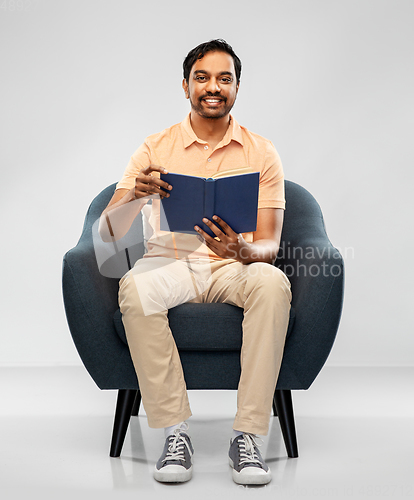 Image of happy young indian man reading book in chair