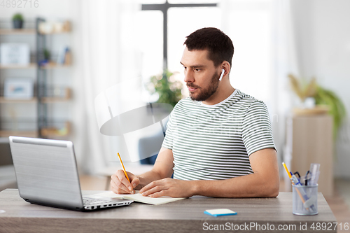 Image of man with notebook, earphones and laptop at home
