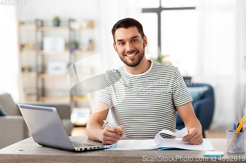 Image of man with papers and laptop working at home office