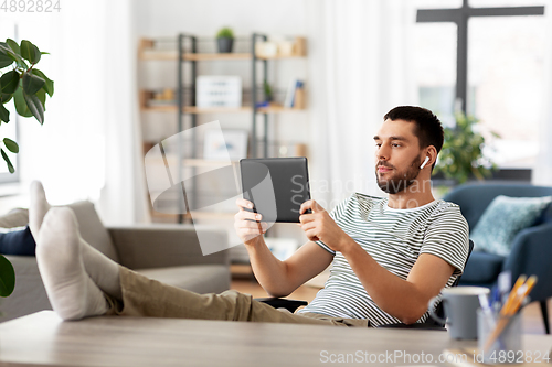 Image of man with tablet pc and earphones at home