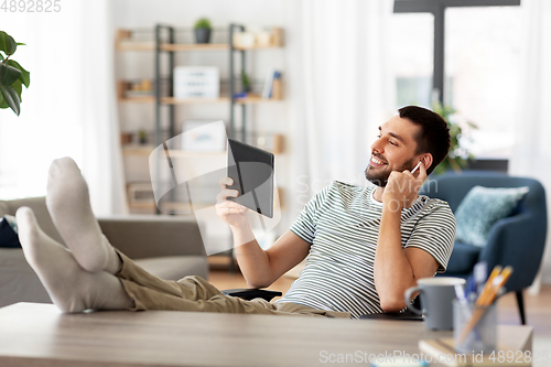 Image of happy man with tablet pc and earphones at home