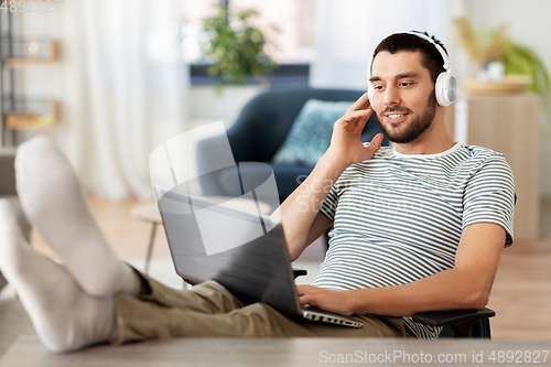 Image of happy man with laptop and headphones at home