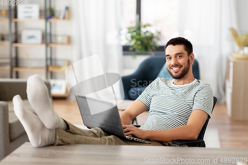 Image of man with laptop resting feet on table at home