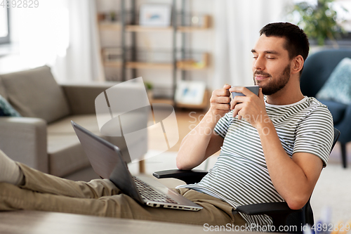 Image of happy man with laptop drinking coffee at home