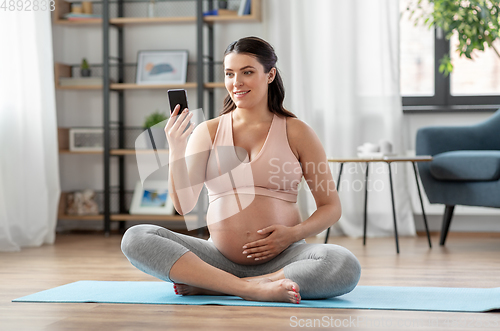 Image of happy pregnant woman with phone doing yoga at home