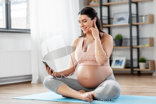 Image of pregnant woman with earphones doing yoga at home