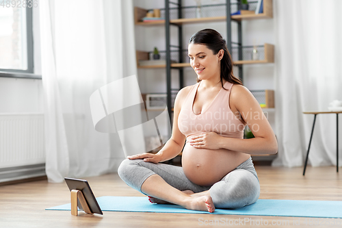 Image of pregnant woman with tablet pc doing sports at home