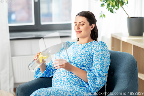 Image of happy pregnant woman drinking fruit water at home