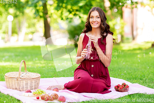 Image of happy woman with picnic basket and drink at park