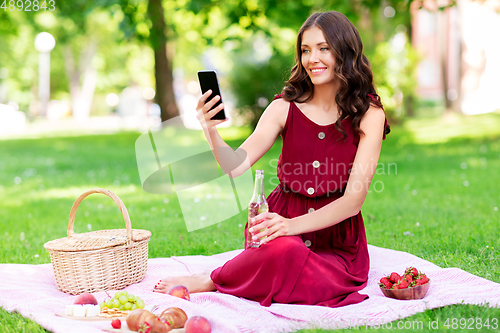 Image of happy woman with smartphone and drink at park