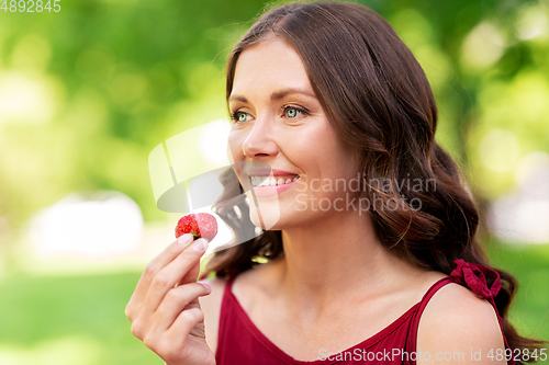 Image of happy woman eating strawberry at summer park