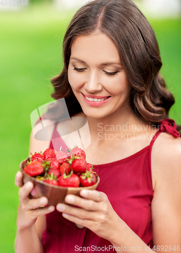 Image of happy woman eating strawberry at summer park