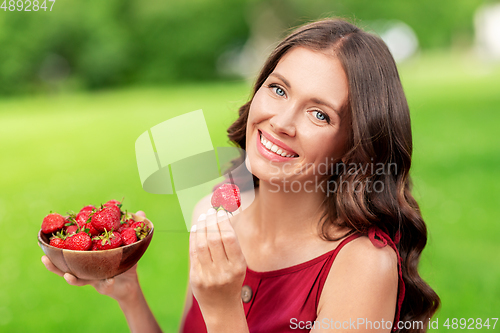 Image of happy woman eating strawberry at summer park