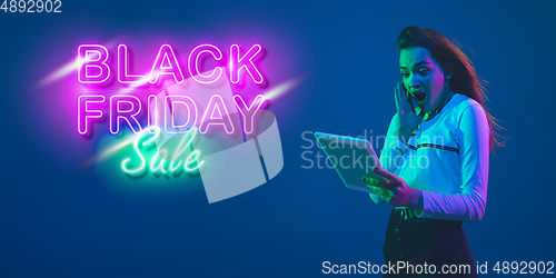 Image of Portrait of young woman in neon light on blue backgound. The human emotions, black friday, cyber monday, purchases, sales, finance concept. Neoned lettering.