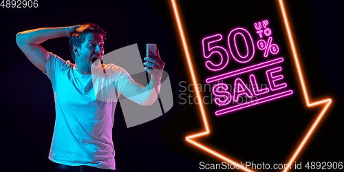 Image of Portrait of young man in neon light on dark backgound. The human emotions, black friday, cyber monday, purchases, sales, finance concept. Neoned lettering.