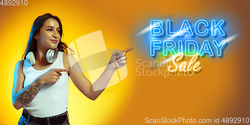 Image of Portrait of young woman in neon light on yellow backgound. The human emotions, black friday, cyber monday, purchases, sales, finance concept. Neoned lettering.