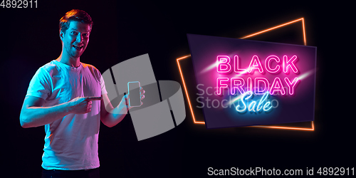 Image of Portrait of young man in neon light on dark backgound. The human emotions, black friday, cyber monday, purchases, sales, finance concept. Neoned lettering.