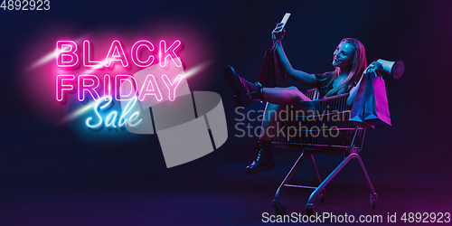 Image of Portrait of young woman in neon light on dark backgound. The human emotions, black friday, cyber monday, purchases, sales, finance concept. Neoned lettering.