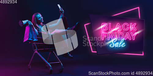 Image of Portrait of young woman in neon light on dark backgound. The human emotions, black friday, cyber monday, purchases, sales, finance concept. Neoned lettering.