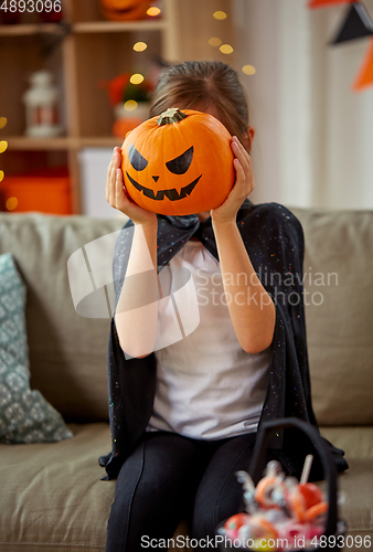 Image of girl in halloween costume with pumpkin at home