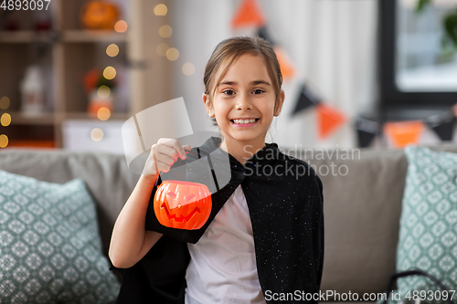 Image of girl in halloween costume with bat cape at home