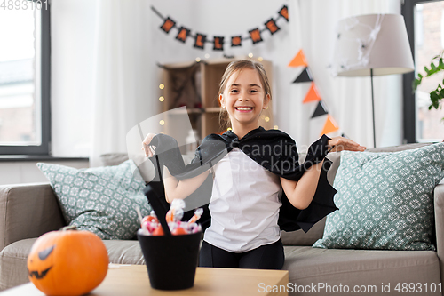 Image of girl in halloween costume with bat cape at home