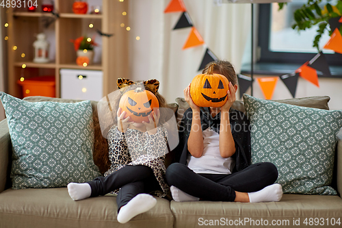 Image of girls in halloween costumes with pumpkins at home