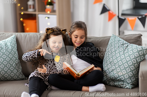 Image of girls in halloween costumes reading book at home