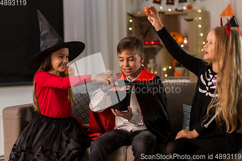 Image of kids in halloween costumes sharing candies at home