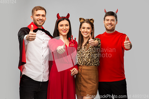 Image of happy friends in halloween costumes snow thumbs up