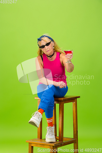 Image of Senior woman in ultra trendy attire isolated on bright green background