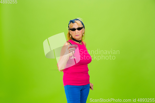 Image of Senior woman in ultra trendy attire isolated on bright green background