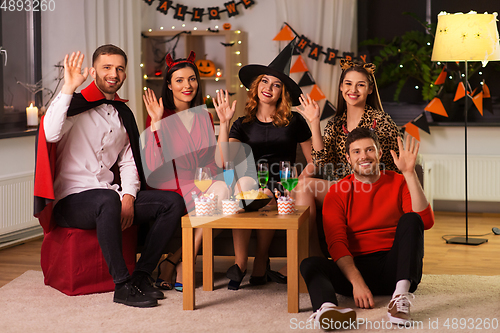 Image of happy friends in halloween costumes at home party