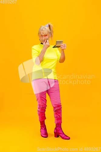 Image of Senior woman in ultra trendy attire isolated on bright orange background