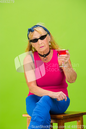 Image of Senior woman in ultra trendy attire isolated on bright green background