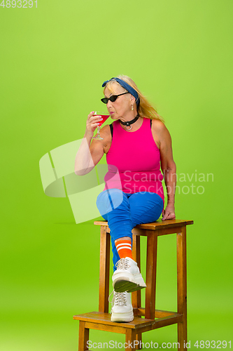 Image of Senior woman in ultra trendy attire isolated on bright green background