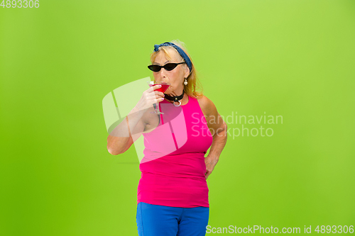Image of Senior woman in ultra trendy attire isolated on bright green background
