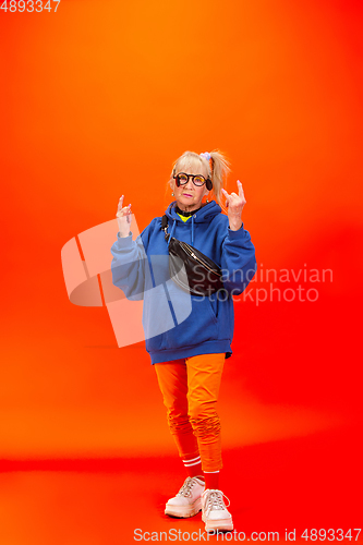 Image of Senior woman in ultra trendy attire isolated on bright orange background