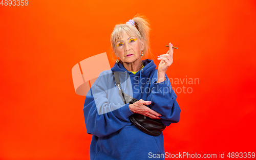 Image of Senior woman in ultra trendy attire isolated on bright orange background