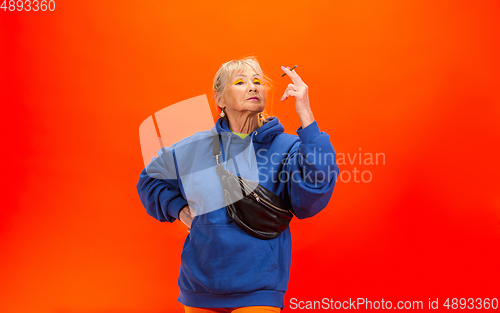 Image of Senior woman in ultra trendy attire isolated on bright orange background