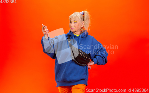 Image of Senior woman in ultra trendy attire isolated on bright orange background