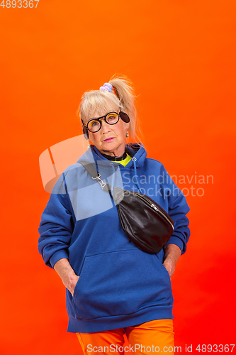 Image of Senior woman in ultra trendy attire isolated on bright orange background