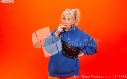 Image of Senior woman in ultra trendy attire isolated on bright orange background