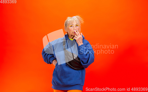 Image of Senior woman in ultra trendy attire isolated on bright orange background