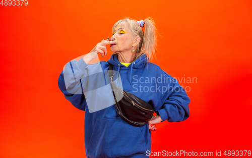 Image of Senior woman in ultra trendy attire isolated on bright orange background